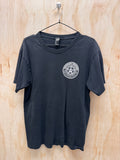 A black short-sleeve t-shirt hanging on a black wire hanger against a light wood panel background. The shirt features a white circular graphic printed on the left chest containing a star design and the text 'SOUTH CAROLINA DEFENSE FORCE'.