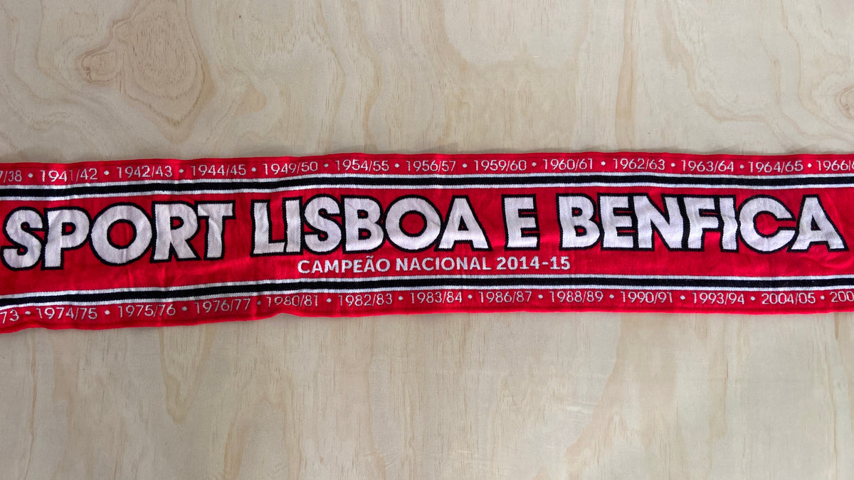 A red fabric scarf with white and black text reading 'SPORT LISBOA E BENFICA' and 'CAMPEAO NACIONAL 2014-15', laid flat on a light wood background.