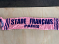 A pink scarf with navy blue text reading 'STADE FRANçAIS PARIS' and matching side stripes, laid flat on a light wood surface.