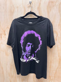A black short-sleeve graphic t-shirt hanging on a black hanger against a light wood panel background. The shirt features a stylized purple and white graphic portrait of Jim Morrison on the front.